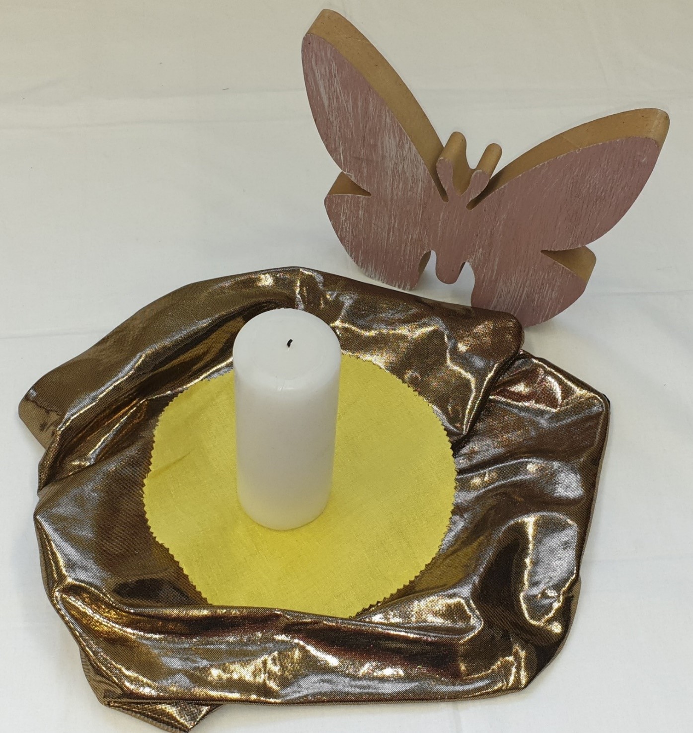 Weiße Kerze auf glänzendem Tuch vor Schmetterlingsfigur aus Holz