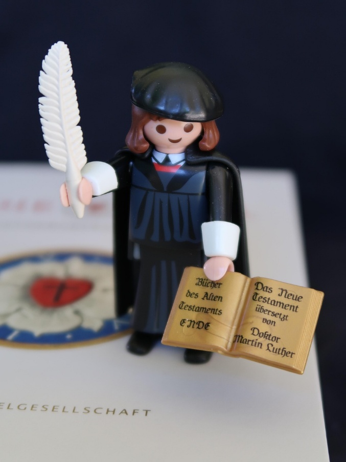 Playmobil-Figur Martin Luther mit Feder und Bibel in den Händen steht auf der Lutherbibel