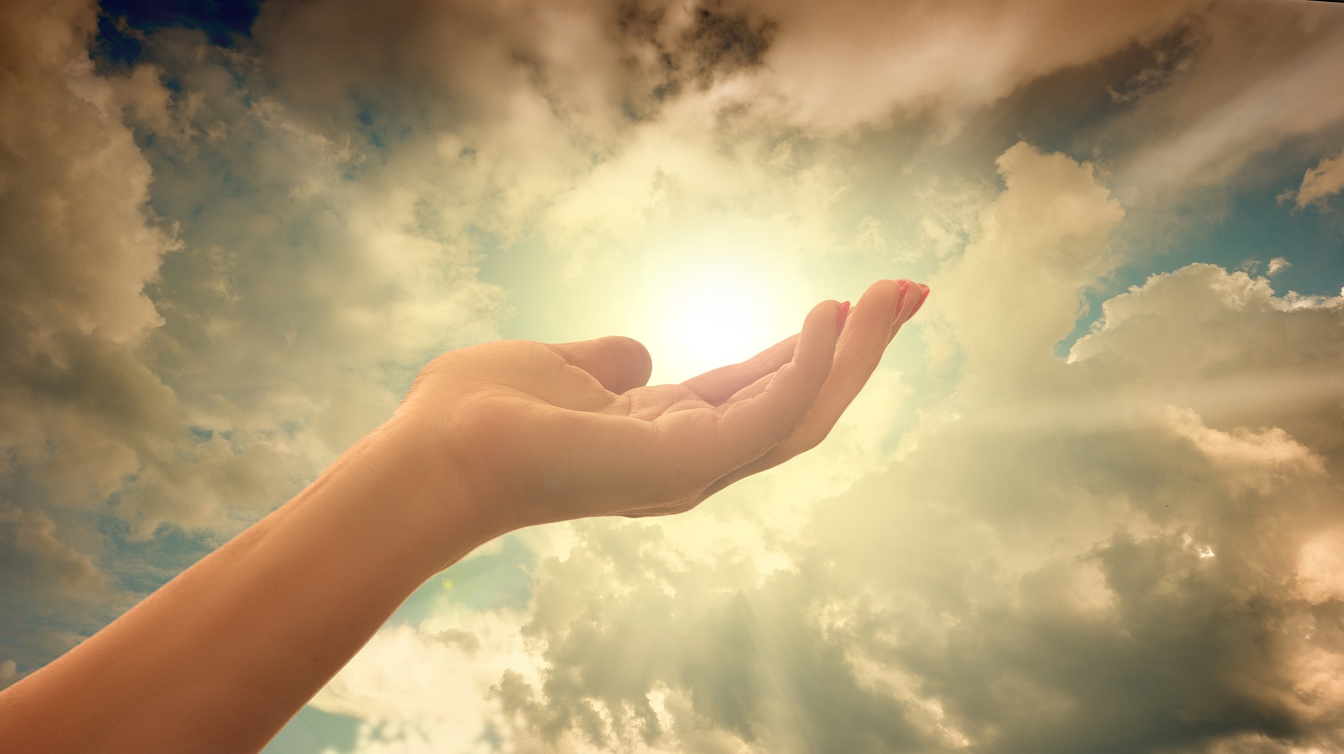 Emporgereckte offene empfangende Hand vor Himmel mit Wolken durch die Sonne scheint
